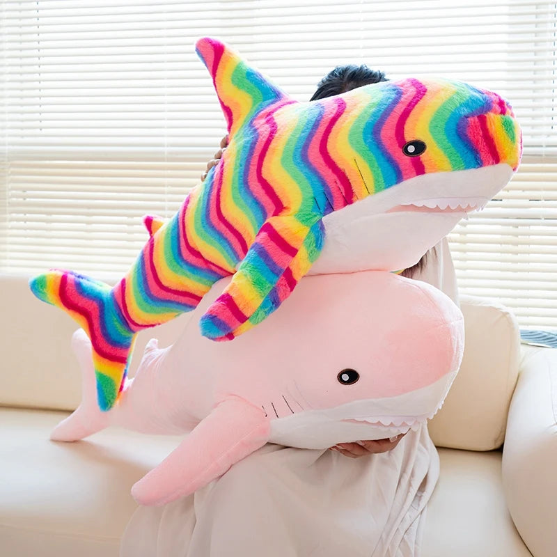 A large plush toy shaped like a shark with brightly colored, striped skin sitting on a person's lap.