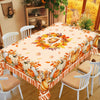 Fall harvest tablecloth featuring orange pumpkins, maple leaves, and autumn foliage on a wooden table.