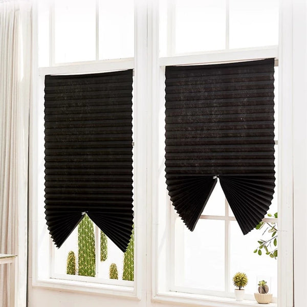 Black non-woven pleated blackout curtains hanging in a white window frame.