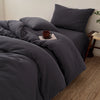 A dark gray duvet cover set with matching pillows and a mug on the bed.