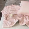 A pink reversible cooling quilt is laid out on a bed with a white pillow and a lit candle.