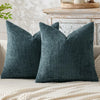 A dark teal chenille pillow cover with a ruffled edge resting on a light-colored blanket.