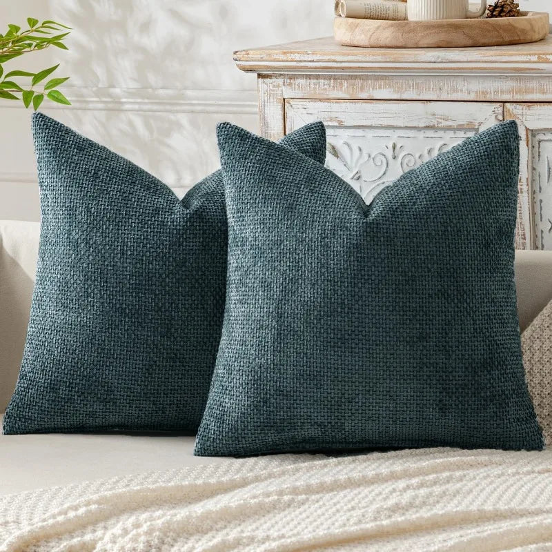 A dark teal chenille pillow cover with a ruffled edge resting on a light-colored blanket.