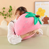 A woman is holding a pink plush strawberry throw pillow with green leaves and a brown stem.