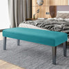 A teal velvet bench slipcover with secure straps placed on a gray striped rug in a bedroom setting.