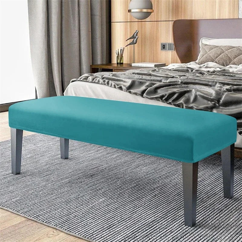 A teal velvet bench slipcover with secure straps placed on a gray striped rug in a bedroom setting.