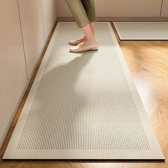 A beige striped kitchen floor mat with a non-slip backing placed on a light wood floor.