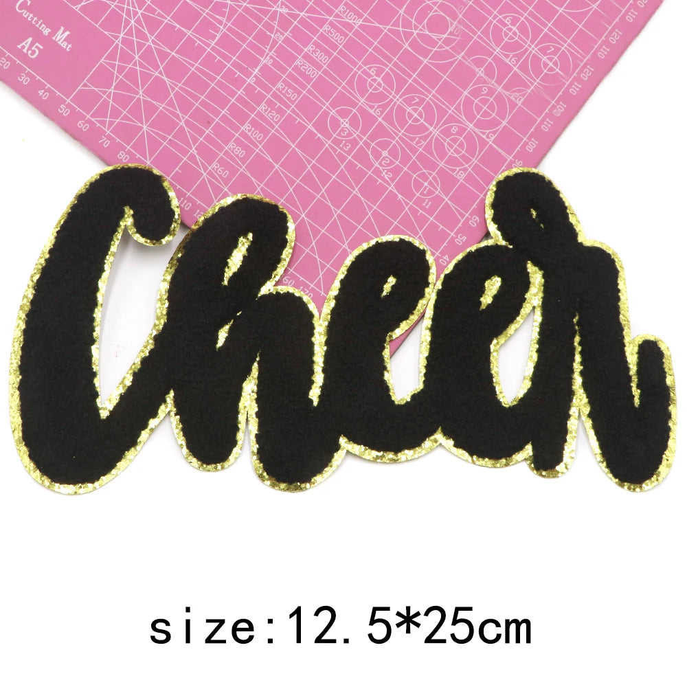 Black felt cheer lettering with gold glitter outline on a pink grid background