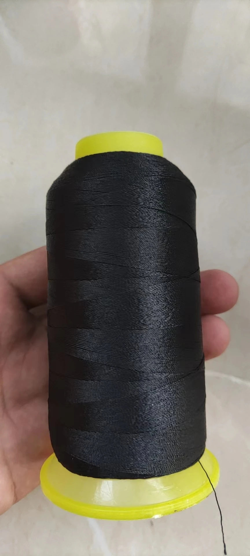 A spool of black high tenacity polyester sewing thread with a yellow core is held in a hand.