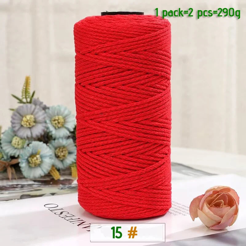A red yarn spool with a black core is shown on a white surface, next to a pink rose.