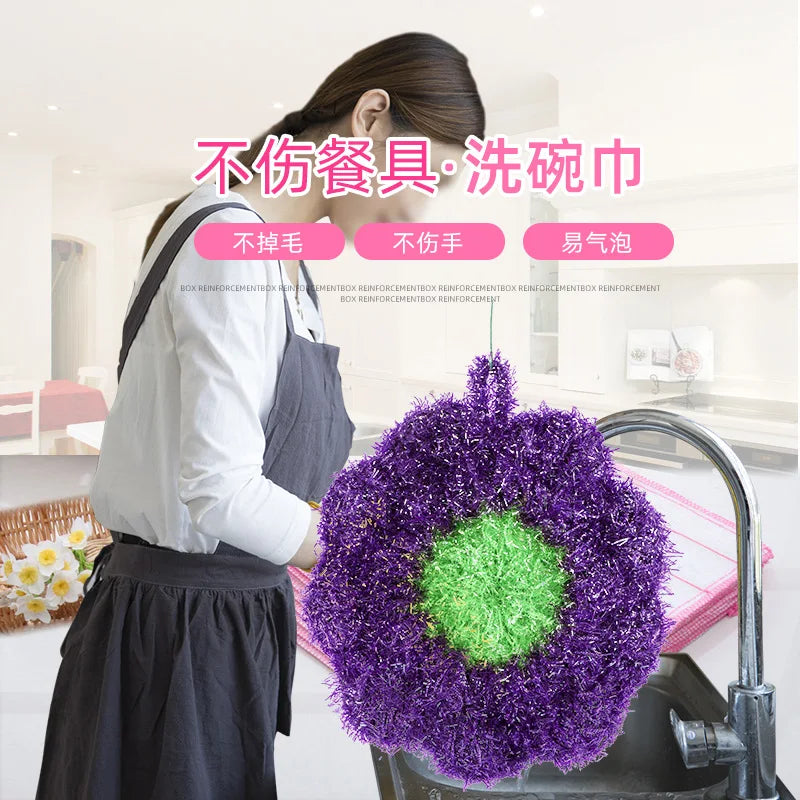 A purple flower-shaped kitchen dish scrubber sponge is shown in a sink.