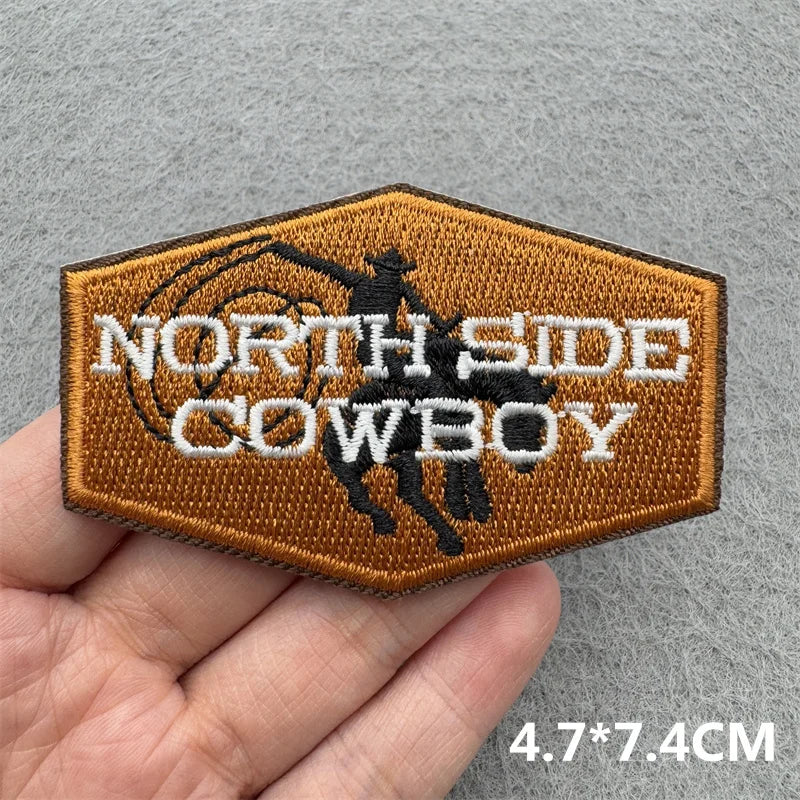 An embroidered patch with the text NORTH SIDE COWBOY on a brown fabric background.