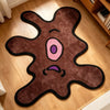 A dark brown, playful one-eye monster shaped area rug with pink and purple features on a light wood floor.