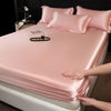A pink satin fitted sheet is draped over a mattress, with pillows and a small tray visible.