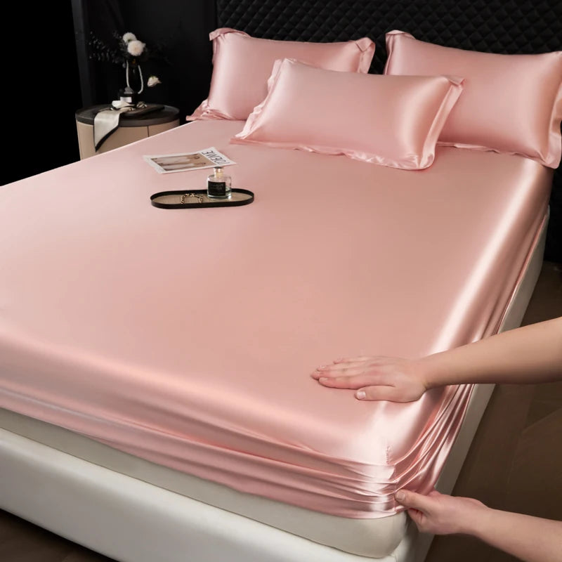 A pink satin fitted sheet is draped over a mattress, with pillows and a small tray visible.