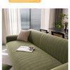 A textured olive green sofa slipcover in a woven pattern shown indoors near a window.