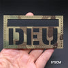 A rectangular tactical flag patch featuring a dark camouflage pattern on a tan fabric, held in a hand.