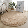 A fluffy beige shaggy round area rug placed on a light wood floor next to a sofa and a framed plant print.