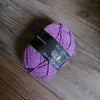 Purple milk cotton knitting yarn skein lying on a wooden surface.