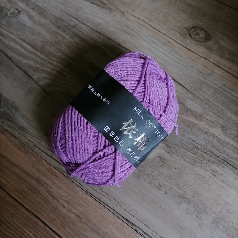 Purple milk cotton knitting yarn skein lying on a wooden surface.