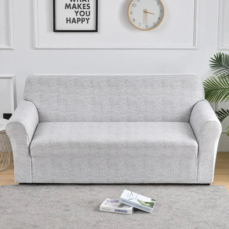 A light gray elastic sofa cover protector placed on a beige carpet.