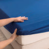 A hand is touching a bright blue waterproof fitted bed sheet on a white mattress.