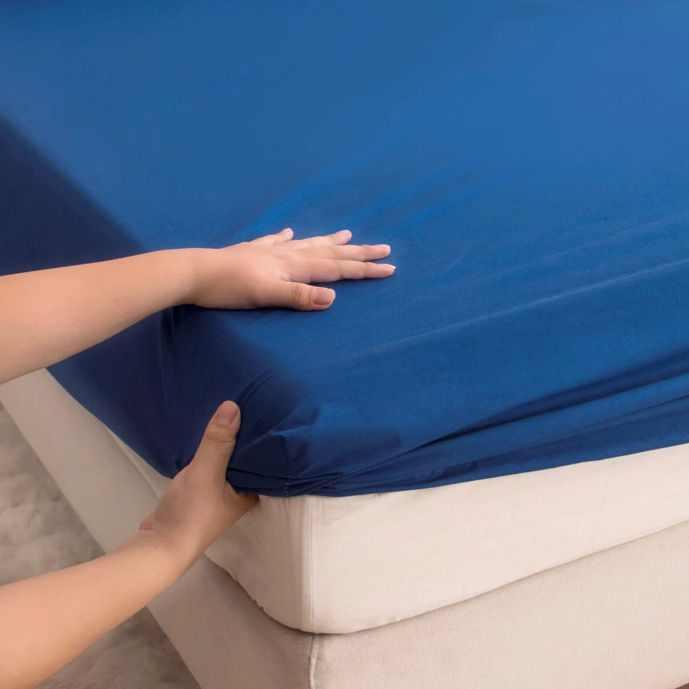 A hand is touching a bright blue waterproof fitted bed sheet on a white mattress.