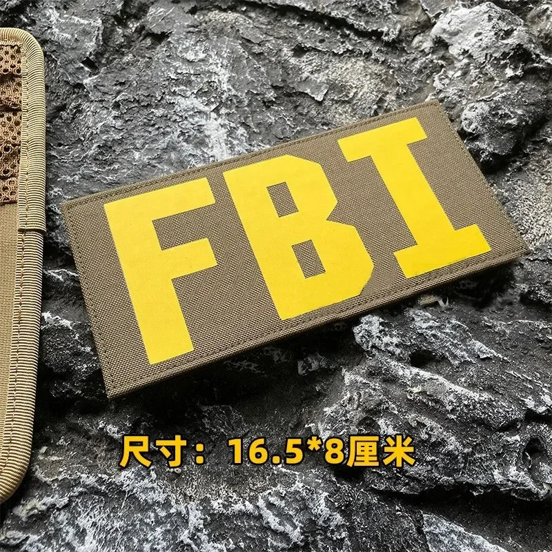 Yellow FBI patch with black stitching on a dark gray rock surface