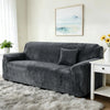 A dark gray stretch velvet sofa slipcover placed in a bright living room with a white rug and framed artwork.