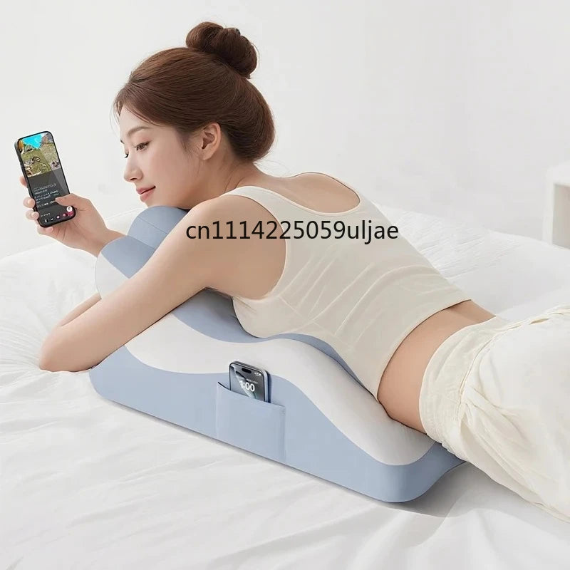 A woman is lying on a white bed using a light blue memory foam body pillow with a phone holder.