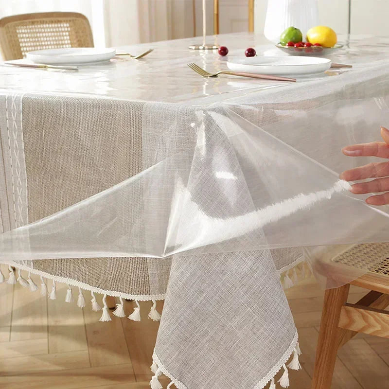 Clear heat-resistant PVC tablecloth protector draped over a light linen tablecloth on a dining table.
