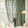 Long, sheer floral lace curtain panels in sage green hanging in a bright room.