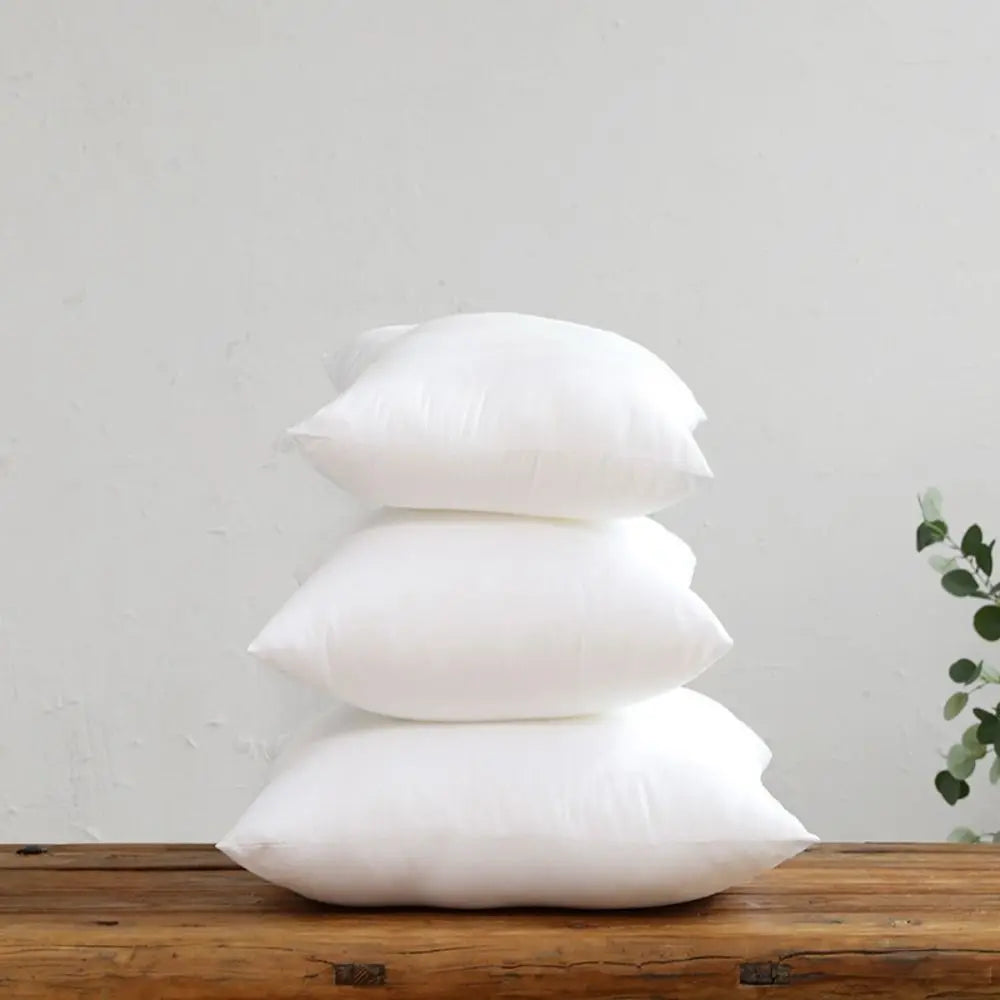 Three white cotton-filled decorative throw pillow inserts stacked on a wooden surface.