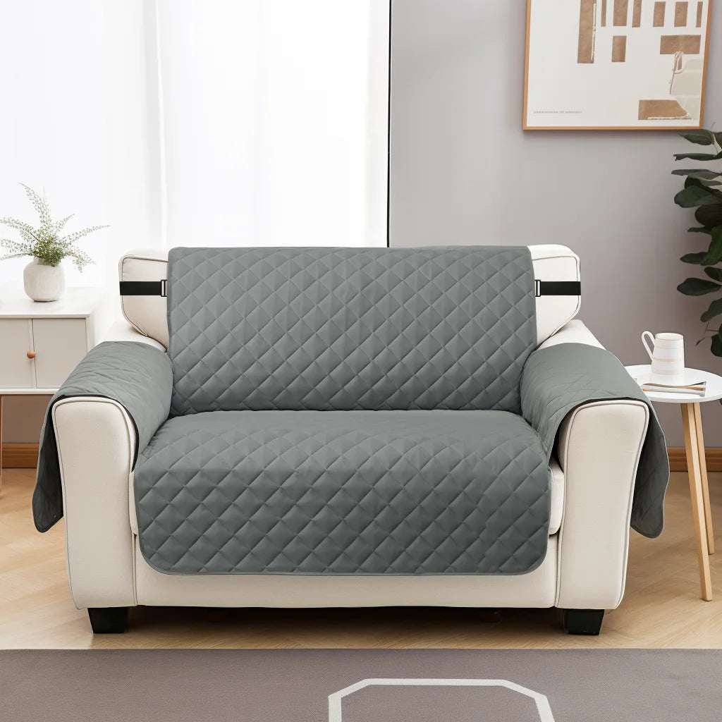 A light gray reversible sofa slipcover in a quilted pattern sitting on a white wooden cabinet.