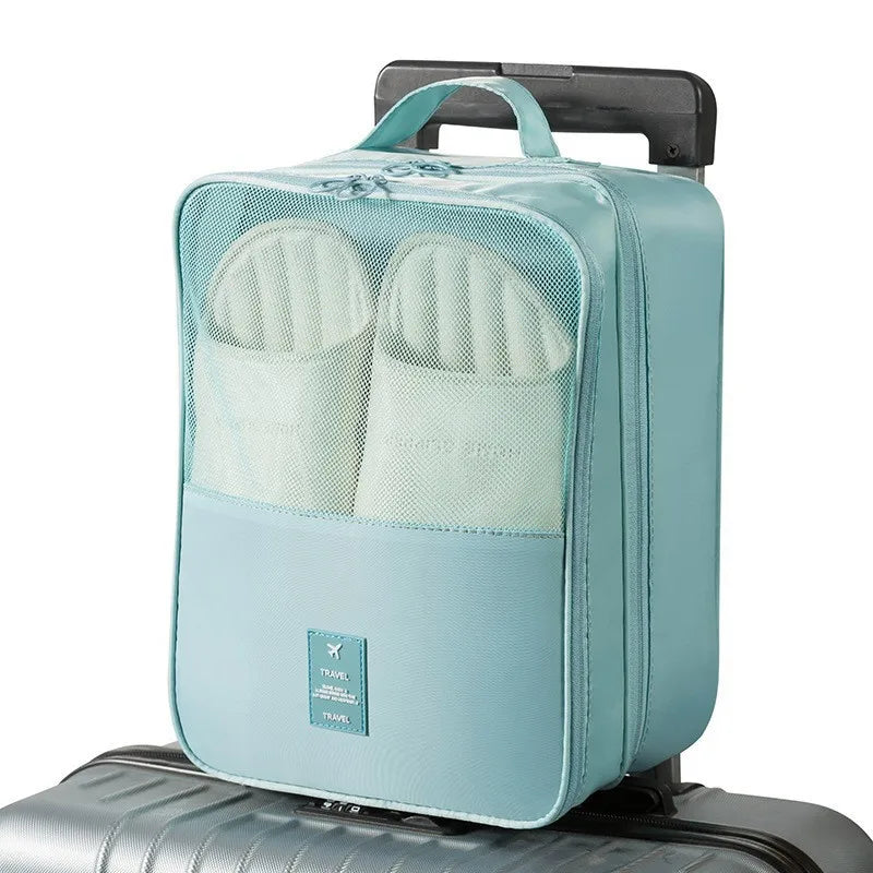 A light blue portable travel shoe organizer bag with a mesh pocket for shoes resting on a silver suitcase.