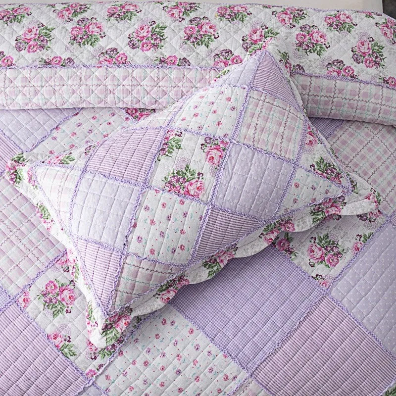 A close-up of a patchwork floral plaid cotton quilt featuring shades of lavender and pink flowers.