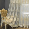 A sheer, embroidered beaded curtain with a punched-hole design hanging in a light setting.