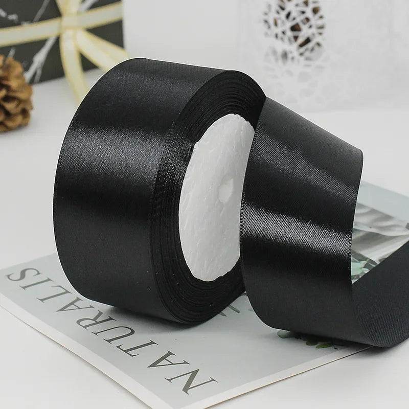 Roll of black satin ribbon with white decorative trim on a white background