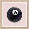A glossy black billiard ball with the number 8 on it, set against a light pink background.