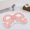 A pink fluffy decorative rug shaped like a bow is displayed next to a silver figurine.