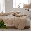 A beige minimalist duvet cover is spread on a bed with white linens and natural light in the background.