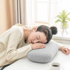 A woman rests her head on a gray memory foam neck and travel pillow indoors.