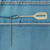 A stainless steel needle threader is shown against a blue denim fabric with white stitching.