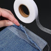 A hand is pulling a piece of denim fabric, showing the edge where heavy duty double-sided iron-on hem tape is applied.