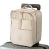 A beige portable travel shoe organizer bag with a handle resting on a silver suitcase.