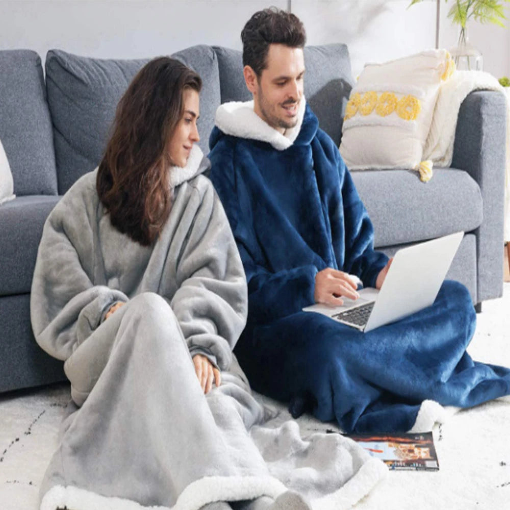A couple relaxing on a sofa wearing oversized flannel blanket pyjama sets.
