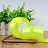 Rolls of fluorescent yellow satin craft ribbons displayed on a wooden surface with green foliage in the background.