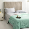 A light green ice silk cooling comforter is displayed on a bed with a neutral upholstered headboard.