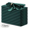 A stack of twelve dark emerald green silky satin dinner napkins with a decorative bow.