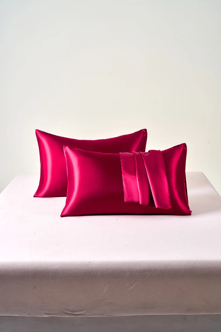 A stack of vibrant magenta satin pillowcases with envelope closures resting on a white table.